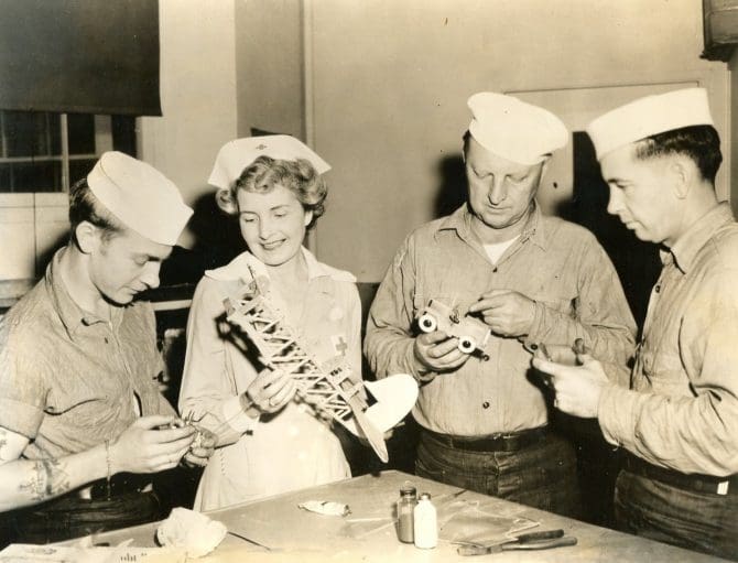 Evelyn Clinick, Gray Lady of the Oakland chapter, examines items made by convalescing soldiers in Red Cross-sponsored hospital arts and skills instruction programs.