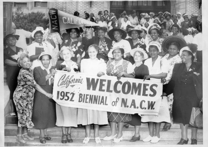 Dozens of members of the National Association of Colored Women gather on a staircase, some holding signs