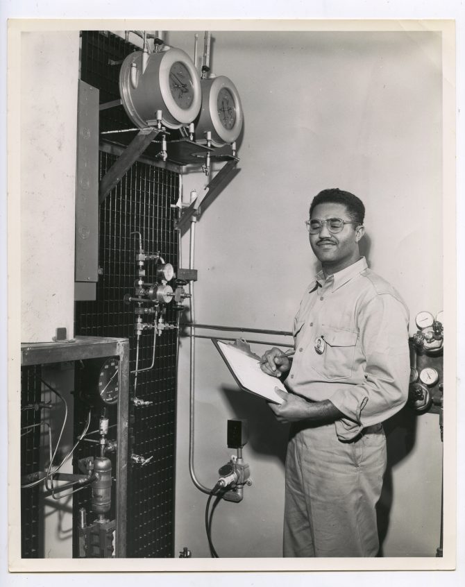 Madison Harvey, Jr. stands with a clipboard in front of some machinery