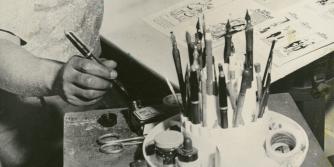 Morrie Turner dips his pen in ink while working on a comic strip at his drafting table