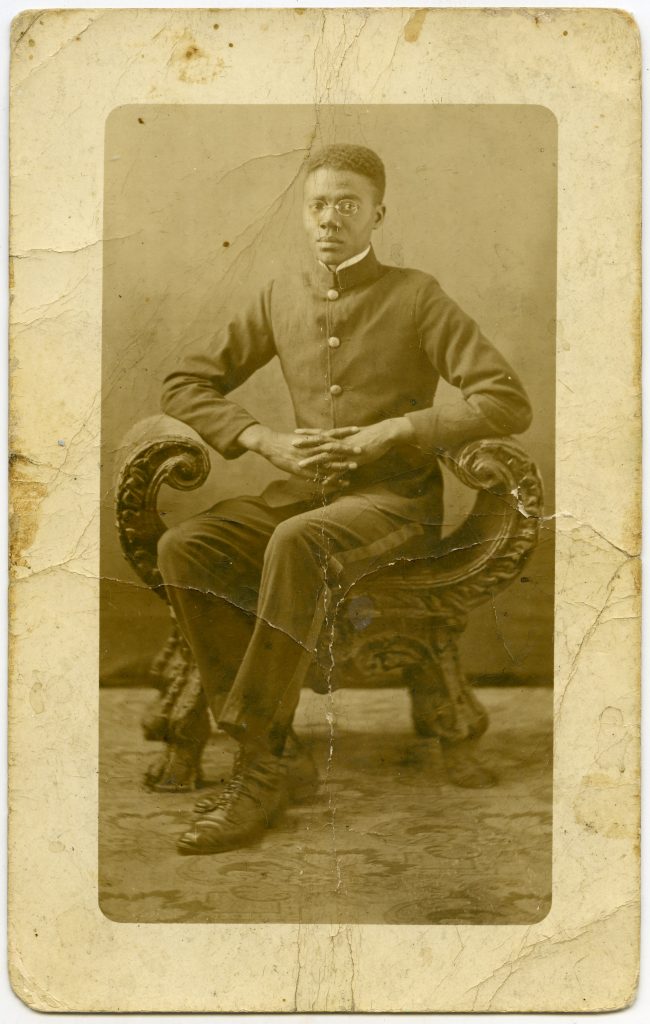 A man in World War 1 soldier's uniform sits on an ornate settee bench