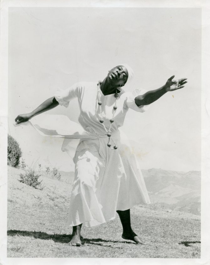 Ruth Beckford dances on a hillside in a white head scarf and dress