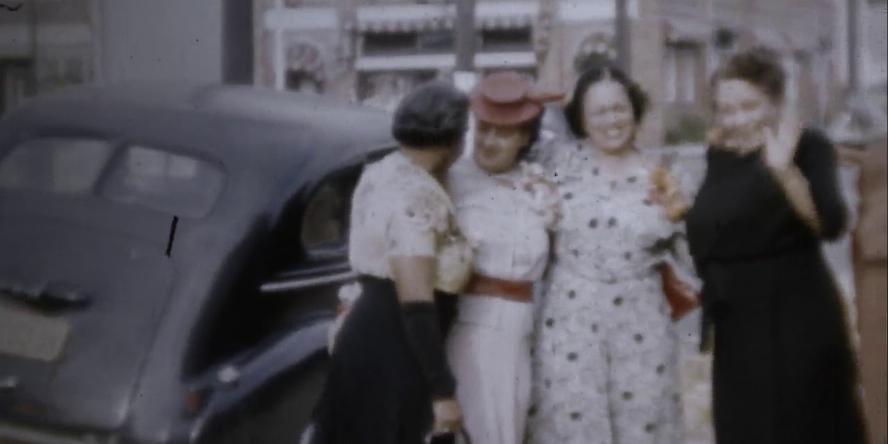 Four women stand nest to an automobile in a still from a home movie