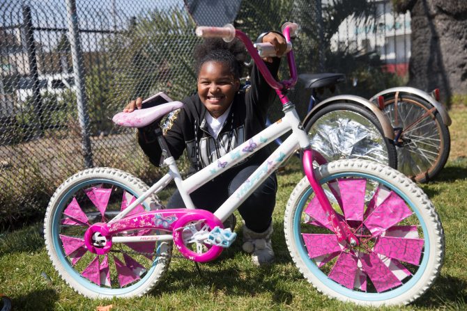 Child squats behind a pink scraper bike, with a huge smile