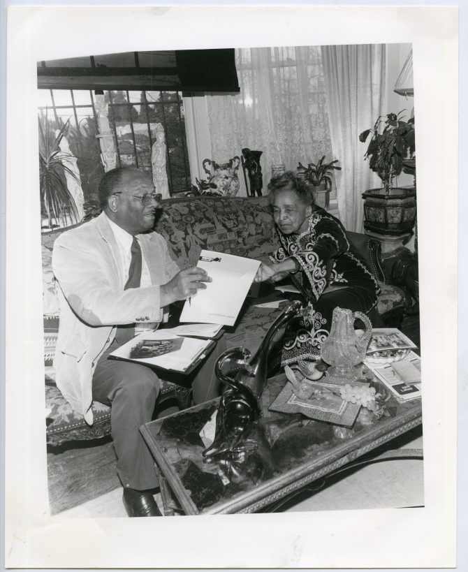 Dr. Lawrence Crouchett and Ida Jackson sitting on couch looking at photographs, 1988, MS32