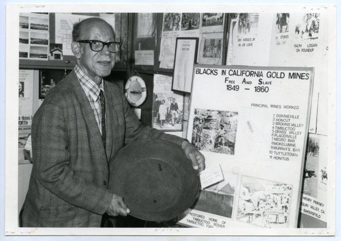 Eugene Lasartemay holding gold pan next to Blacks in California Gold Mines exhibit, circa 1970s, MS32