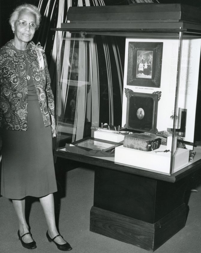 East Bay Negro Historical Society co-founder Marcella Ford standing next to exhibit on William Shorey circa 1970s