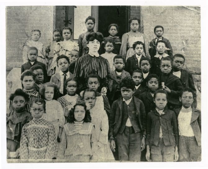 Mary J. Sanderson and class standing in front of school house