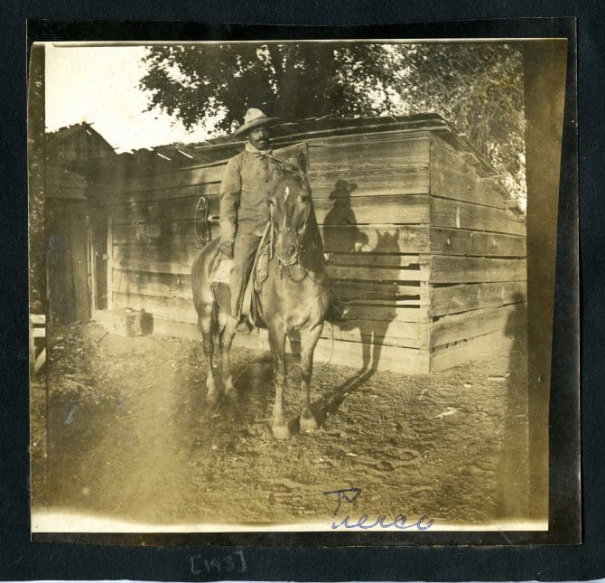 Black cowboy riding a horse next to farm shed, caption: 'Pierce'