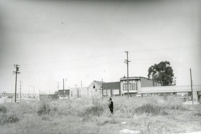 Managing editor of Oakland Post standing in vacant lot overgrown with weeds at 7th and 5th streets in Oakland