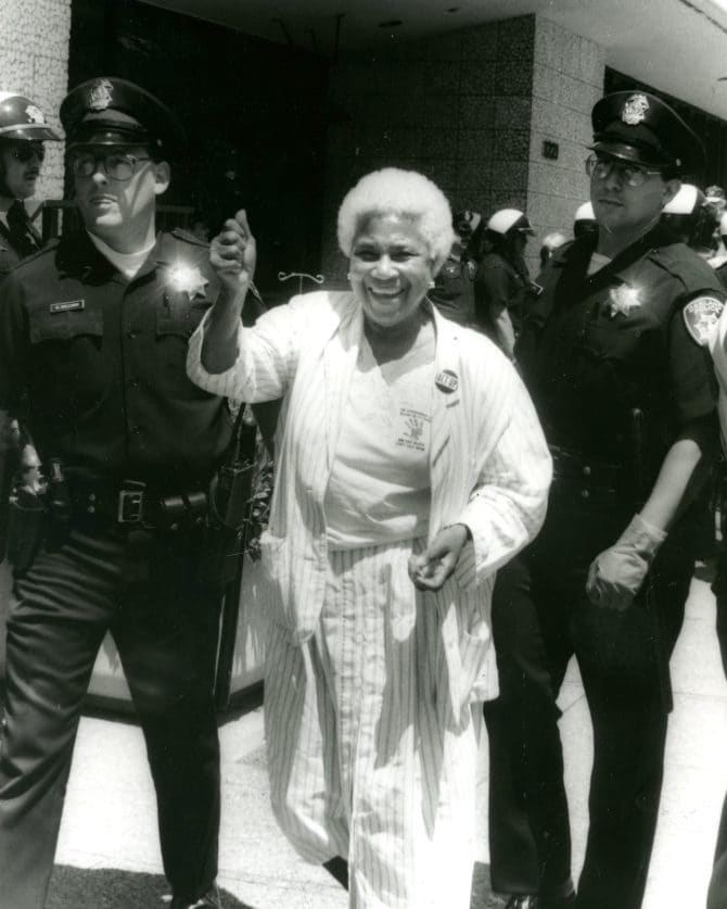 Berkeley city council member Maudelle Shirek being arrested by police officers during ACT-Up East Bay protest rally against High Hospital cutbacks in front of the Alameda County Administration building, 1990