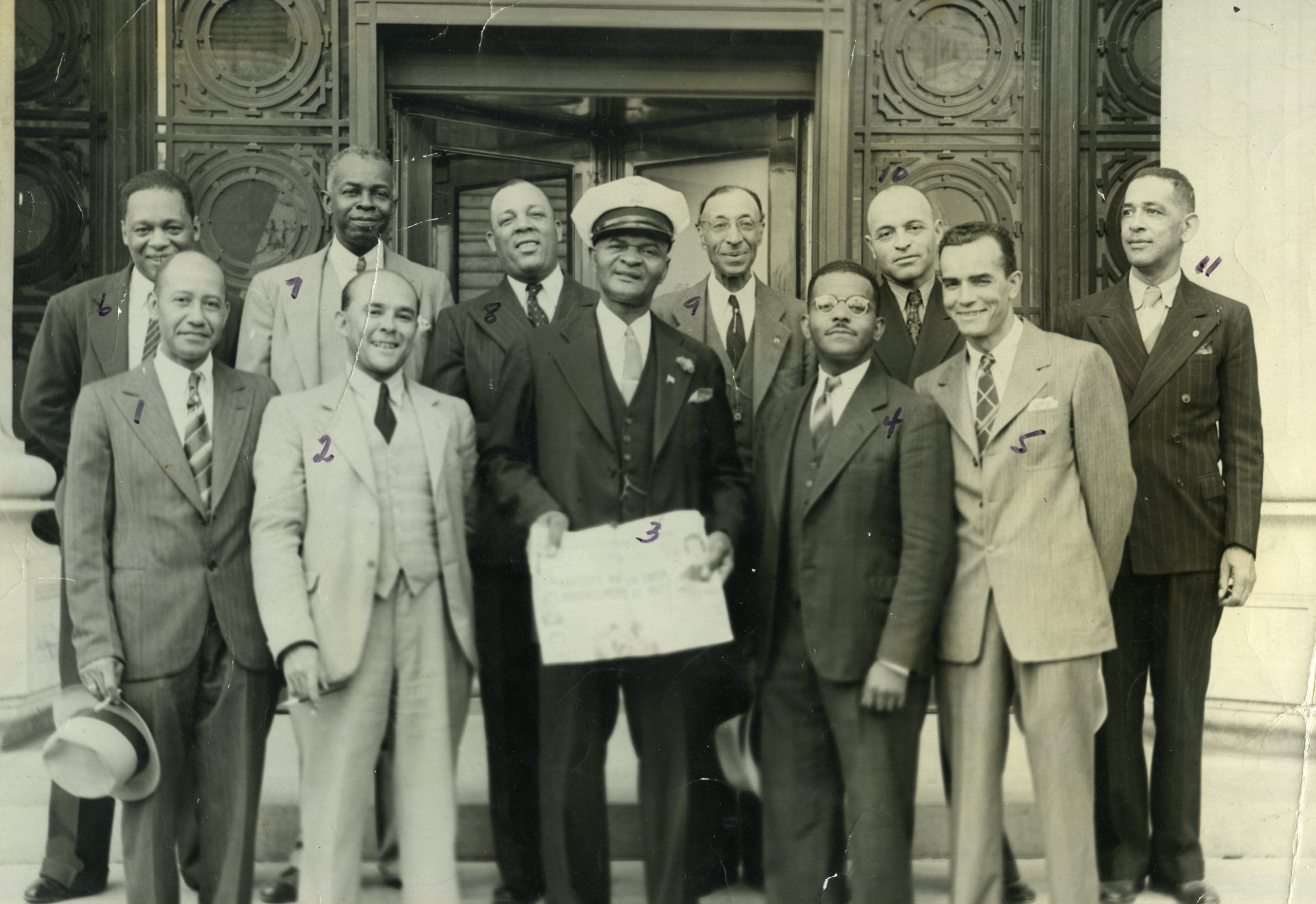 John A. Wilds , first Black Oakland City Hall employee and first Black to run for Oakland City Council, stands with group of men in front of Oakland City Hall holding newspaper