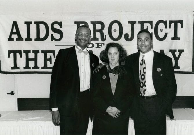 Robert Scott and man and woman standing in front of AIDS Project banner