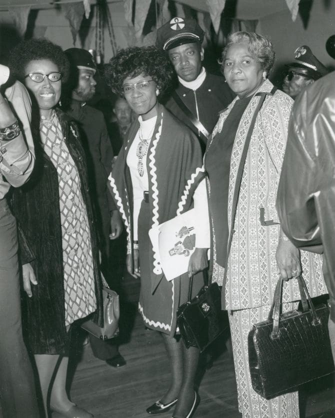 Six members of the local Black Security Guards organization surround Congresswoman Shirley Chisholm during her visit to Berkeley's Rainbow Sign where she discussed her candidacy for president