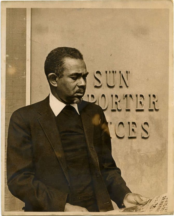 Carlton Goodlett reading newspaper in front of the Sun Reporter office building