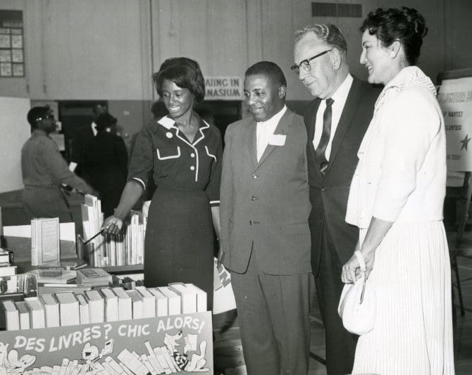 Rosemary Prince, Supervising Librarian of the Elmhurst Branch Library, shows Mayor William L. books on display at the Bay Area Urban League Join In event held at Madison Junior High School