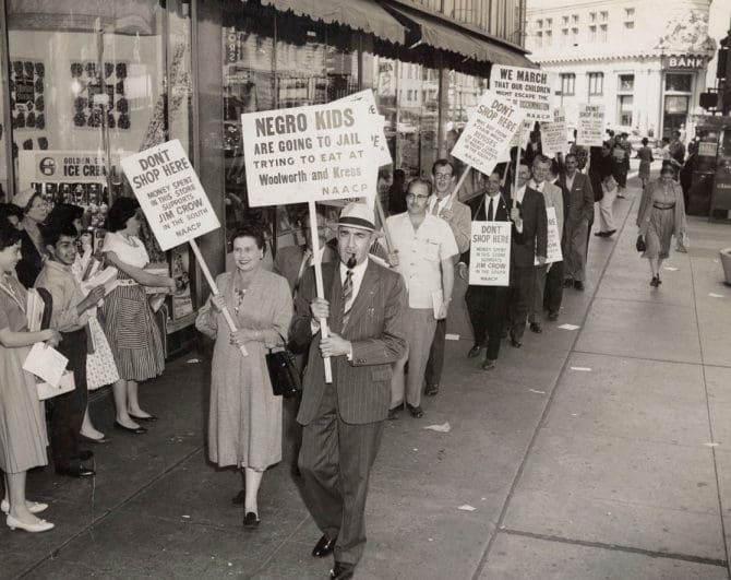 .L. Dellums stands in picket line holding sign, "Negro kids are going to jail trying to eat at Woolworth and Kress"