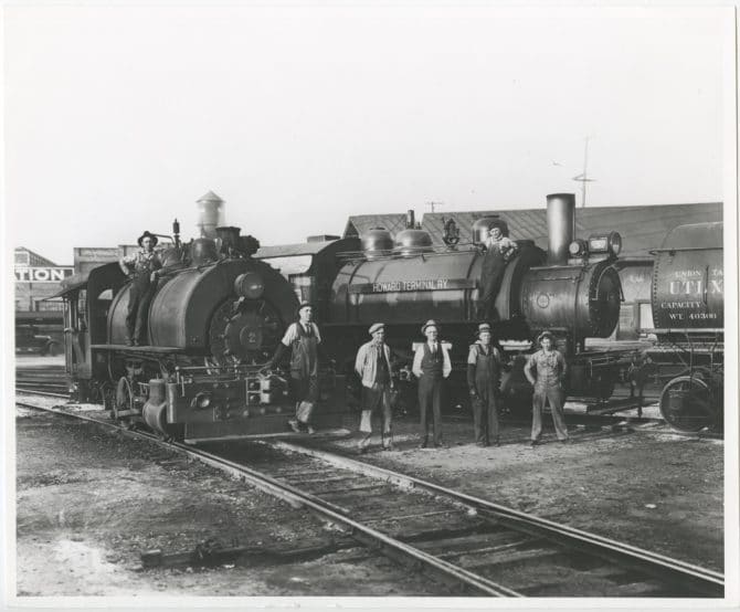 Engineers and crew pose in front of a pair of Howard Terminal Railway trains.