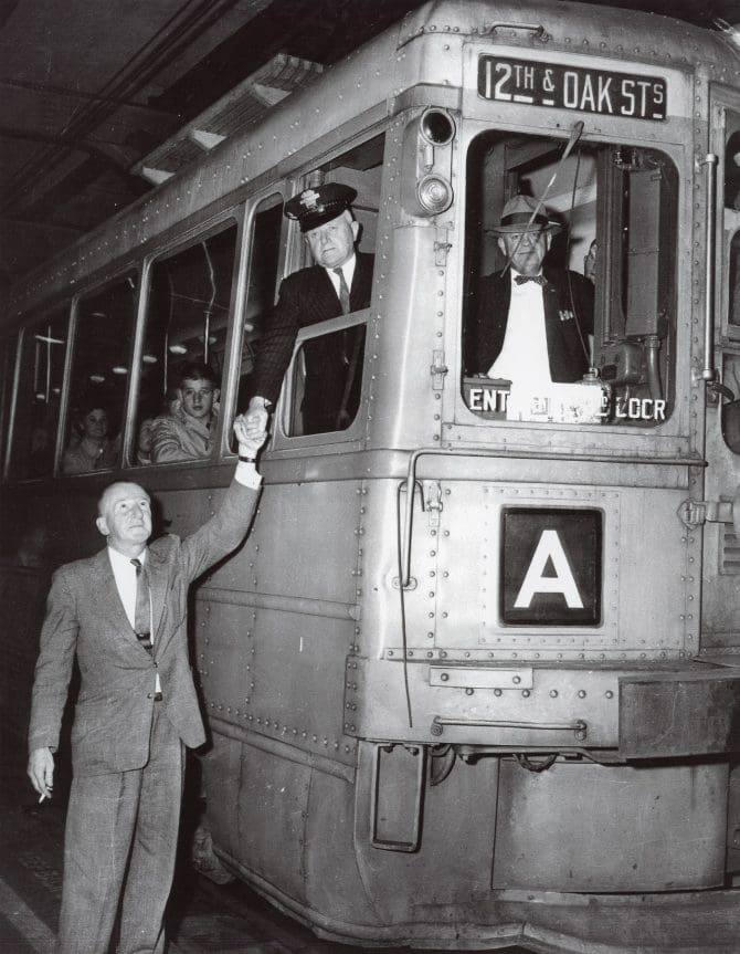 Black and white photo of a passenger reaching up to wave at the driver of the A train to 12th and Oak Streets.