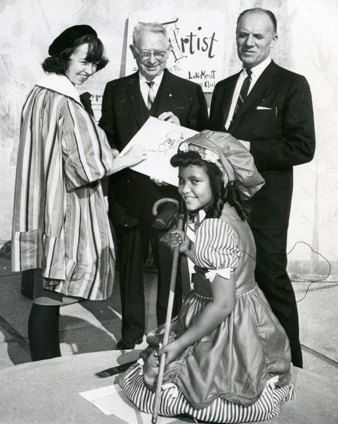 Little Bo Peep (Ruth Broussard) poses as Children's Fairyland artist Marilynn O'Hare sketches her as Dr. Herman Katz and Robert Elsocht look on circa 1965