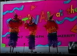 Image from a video of the Festival at the Lake's 1992 Young Artists Stage showing three children walking on stilts and wearing colorful clown costumes.