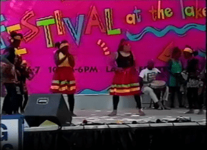 Image from a video of the Festival at the Lake's 1992 Young Artists Stage showing barefoot teenage dancers in brightly colored skirts, with a drummer in the background.
