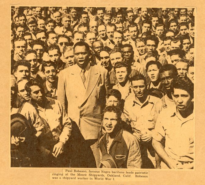 Paul Robeson standing in the midst of a dense crowd of shipyard workers, singing.
