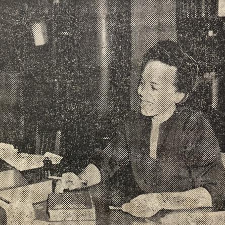 Newspaper clipping showing a man standing at a reference desk receiving help from a librarian.