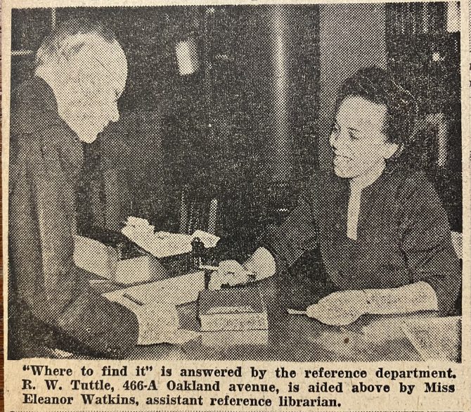 Newspaper clipping showing a man standing at a reference desk receiving help from a librarian.