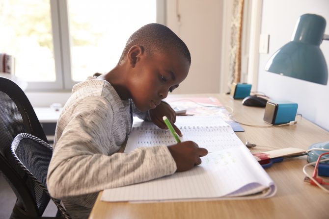 Young Boy In Bedroom Sitting At Desk Doing Homework