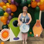 A CPL patron poses with cardboard cut outs and a CPL yard sign in front of a balloon arch at the summer kick off party
