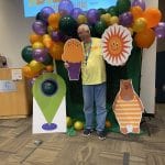 A CPL employee poses with cardboard cut outs in front of a balloon arch at the summer kick off party