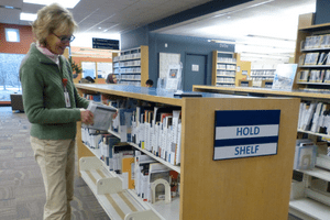 A female CPL staff member smiles as she shelves a book onto Canton Public Library's hold shelf