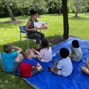 A CPL librarian reads a story to a group of young children outside in the library's backyard