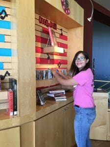 Image of a young girl in pink shirt and blue jeans volunteering at the library assisting with the Rock n Roll display.