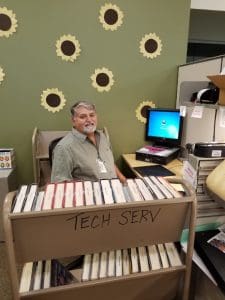 Male volunteer sitting in front of a computer processing items from a cart.