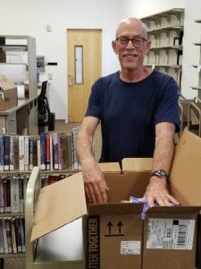 Male volunteer with glasses in a blue shirt unpacking and packing materials.