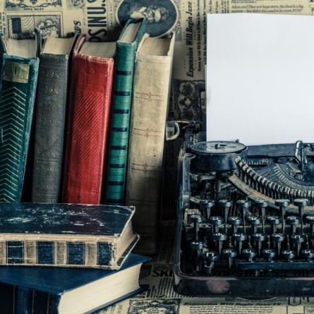 Máquina de escribir antigua con pluma y libros.