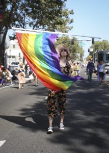 Photograph of a young person walking in a parade joyfully twirling a rainbow flag.