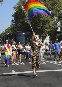 A joyful individual waves a giant rainbow LGBTQ Pride Flag ahead of marching San Jose Public Library staff in the 2019 Silicon Valley Pride Parade.