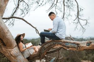 A photo of a man and a woman sitting in a tree reading to each other.