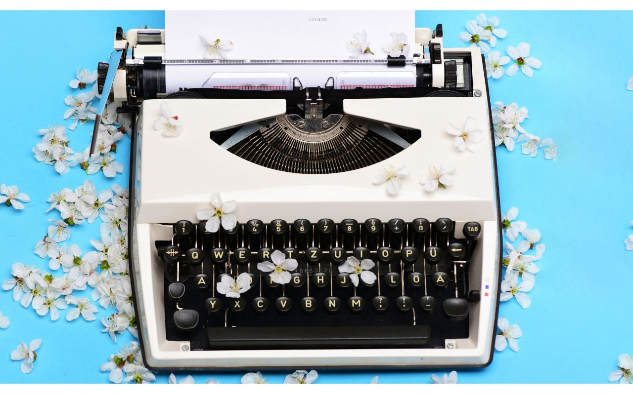 Typewriter surrounded by fallen cherry blossoms on a light blue background