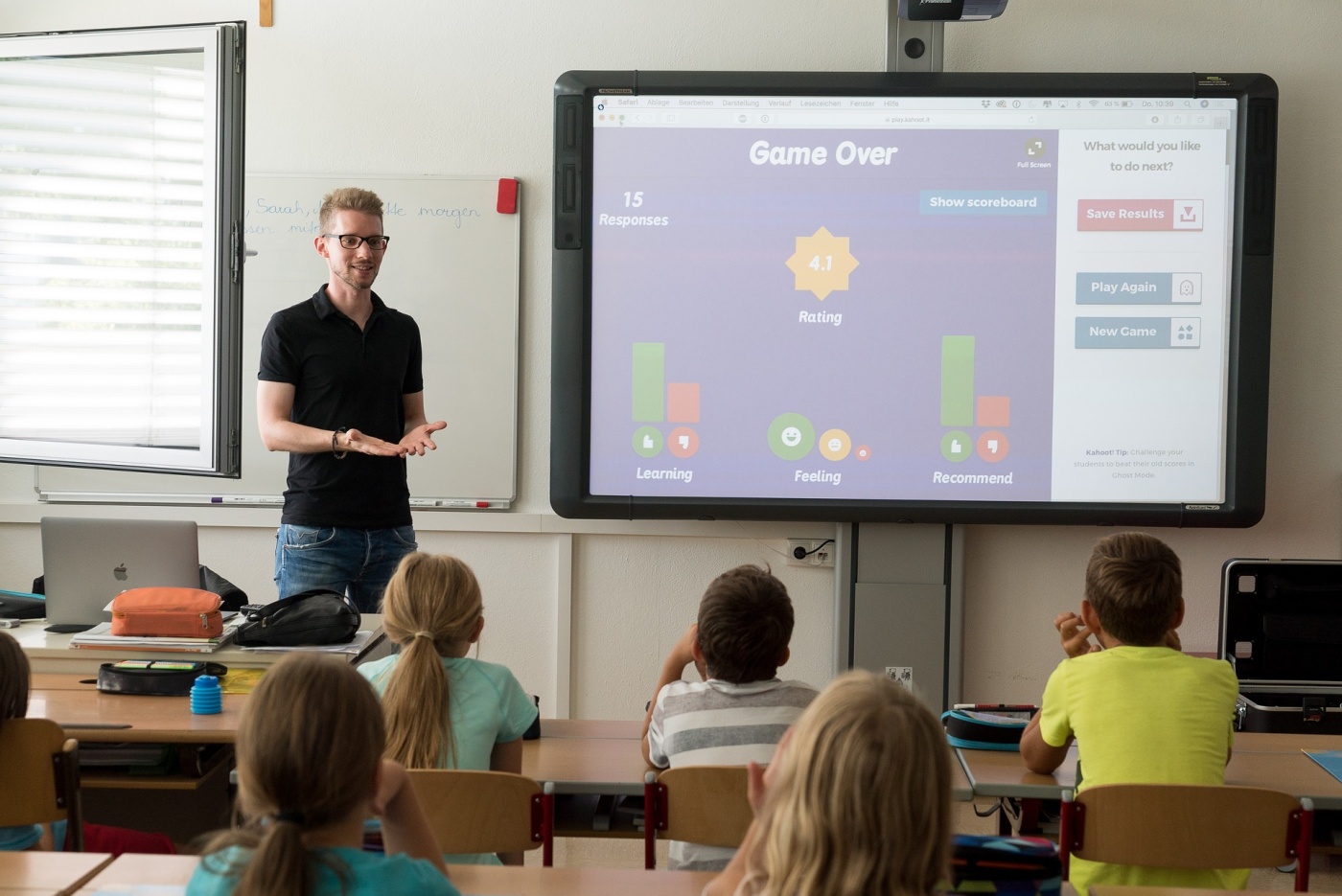 a teacher beside a large display screen in front of students