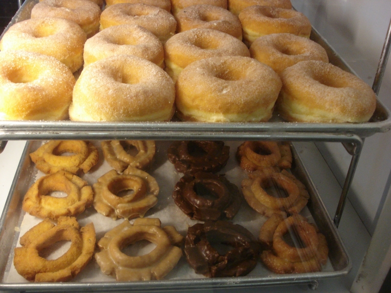 A tray full of fresh old fashioned donuts (lower shelf) at Hooz Donuts. The old fashioned varieties (from left) are plain, maple, chocolate, and glazed.