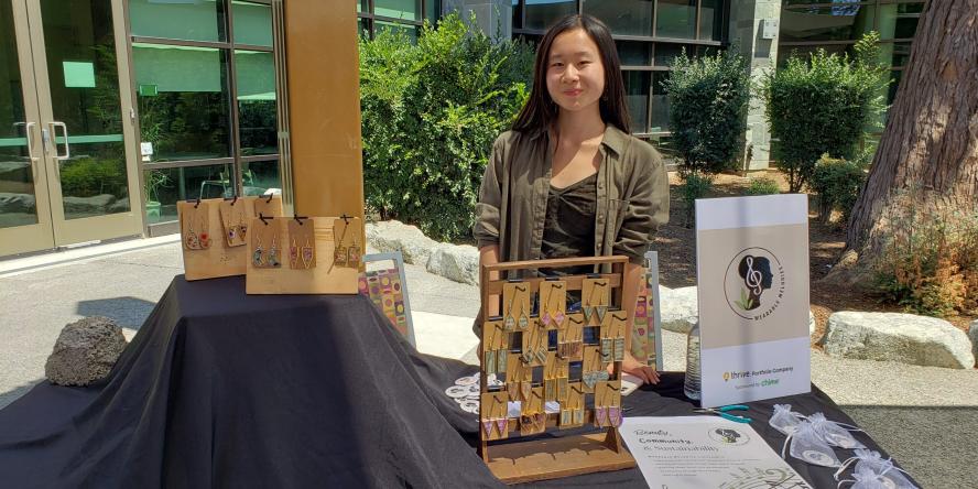 Teen stands behind her black table cloth booth where she is selling earrings