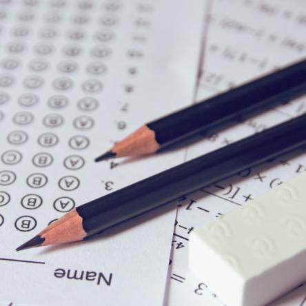 Hoja de respuestas de opción múltiple de prueba estandarizada con dos lápices morados y un borrador blanco.