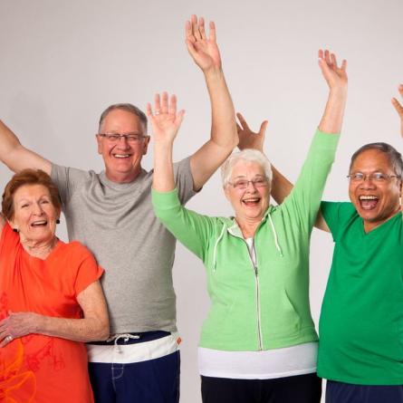 Four senior citizens raising hands in the air cheerfully.