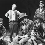 five men in rugged clothing pose on a stage