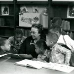 Children with books gather around woman