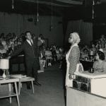 man and two women on stage with audience pictured behind